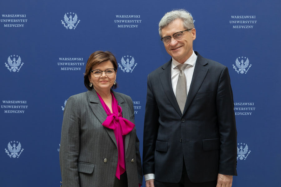 A man and woman dressed elegantly pose for a photo against a banner with the WUM logo