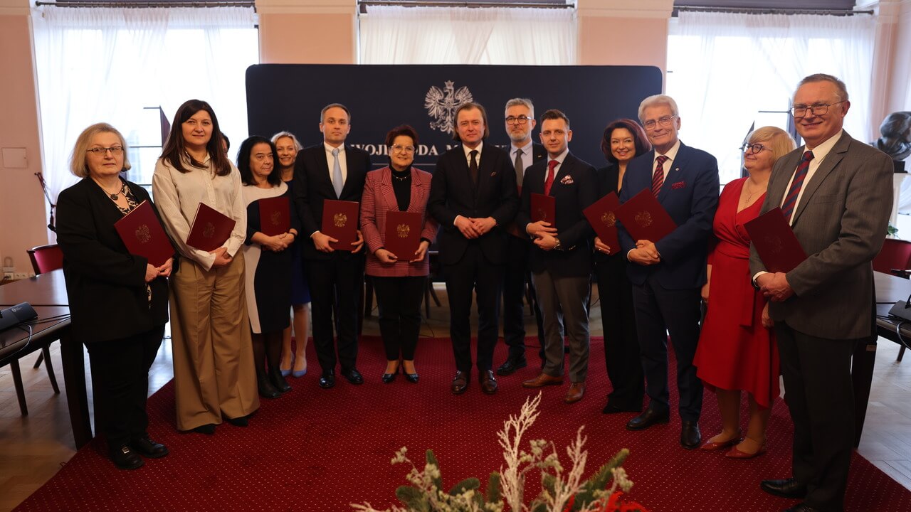 Powołani konsultanci wojewódzcy. Grupa osób w eleganckim pomieszczeniu. Uśmiechają się do zdjęcia. Trzymają w rękach teczki.