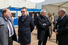 Four men in overcoats, talking to each other on a construction site