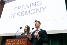 Studenci: kobieta i mężczyzna. Stoją za mównicą i prowadzą galę. Za nimi ekran z napisem Opening Ceremony.