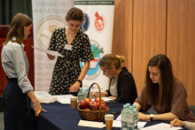 Grupa kobiet, część siedzi przy stole, część stoi. Za nimi rollup konferencji.