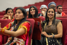 Audience. Many people are sitting on red seats - they are students of various countries in folk costumes. In the foreground are two young girls in colorful costumes.