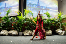 A woman in a bright red outfit and high headgear dances with her hands raised.