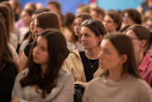 Young people sitting on chairs, listening to a lecture. In the foreground are two young girls. 