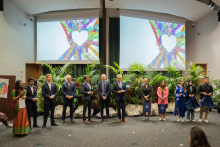 Twelve people stand on the stage. One next to the other. Most are men in suits.