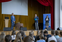 A man in a suit and two high school students in school uniforms stand at the lectern.