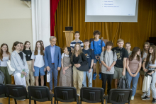 An older man in a blue suit stands with a group of young people. They pose for a photo.