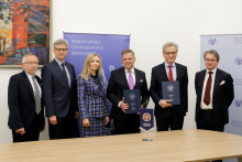 There are six people behind the table. Five men in suits and a woman in a blue plaid suit.