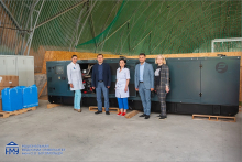 Five people - three women and two men pose for a photo against the backdrop of a power generator.