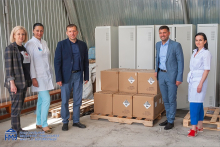 Five people - three women and two men - stand in a warehouse by cardboard boxes.