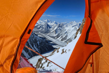 The view from the orange tent over the snow-capped mountain ranges. Blue sky in the background.