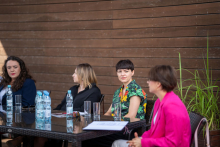 Four women sitting at a table. The woman on the right is turned sideways to the camera, she says. 