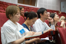 Lecture hall, on the chairs sit young people mostly of Asian.