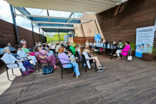 A group of people sitting on chairs, opposite a table behind which sits a group of people - speakers.