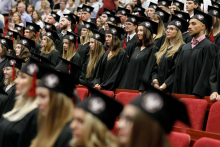 Uroczystość wręczenia dyplomów ukończenia studiów. Młodzi ludzie w czarnych togach i biretach.