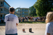 Na pierwszym planie dwie osoby odwrócone tyłem. W oddali grupa młodych osób.