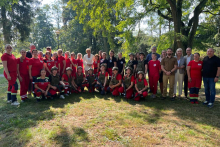 A group of people lined up in a semicircle. First and foremost are women. Those in the first row squatting have bulletproof vests, helmets and weapons. Those in the second row are standing - most dressed in red outfits. 