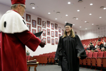 A man in a red toga congratulates a woman in a black toga.