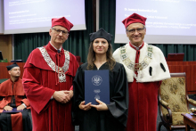 Three people in togas pose for a photo. Two men in red, a woman in black.