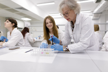 Two young girls and an older woman in white aprons in an analytical laboratory.