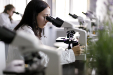 A young girl in a white apron at the microscope.