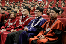 Aula. Wiele osób w togach i biretach siedzi na krzesłach, Na pierwszym planie czterech dziekanów.