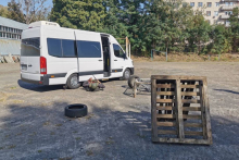 Na parkingu stoi samochód dostawczy obok leży żołnierz z karabinem w ręku.