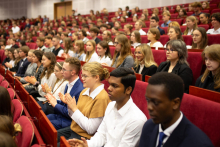 A group of young people dressed smartly sit in rows of red chairs