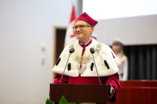 A middle-aged man with glasses stands behind the lectern and speaks.