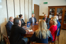 Osiem osób siedzi przy okrągłym stole. Rozmawiają ze sobą.