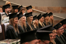 A group of people dressed in academic attire and birettas look ahead, smiling.