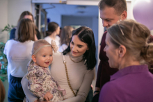 Kobieta z małym dzieckiem na rękach, obok stoi mężczyzna i jeszcze jedna kobieta ubrana w fartuch medyczny.