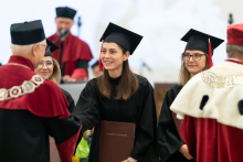 A group of people dressed in black academic togas and a man dressed in a white and red toga and a man dressed in a white and black toga present diplomas.