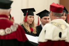 A group of people dressed in black academic togas and a man dressed in a white and red toga and a man dressed in a white and black toga present diplomas.