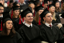 A group of young people, men and women, dressed in black academic togas, look in one direction.