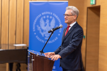 An older man in a suit at the lectern. He speaks into the microphone.