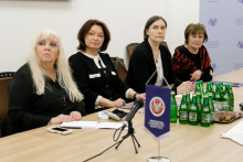 Four women, sitting at a table. In front of them are documents and a WUM pennant.