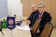 Two men sitting at a table. On the table, documents and a WUM pennant