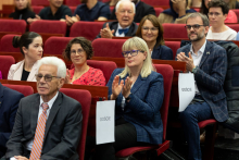 Grupa osób, elegancko ubranych, siedzą w auli wykładowej, patrzą przed siebie.