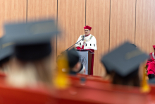 Absolwenci analityki medycznej odebrali dyplomy. Mężczyzna - rektor uczelni, ubrany w oficjalną togę, przemawia, stojąc za mównicą.