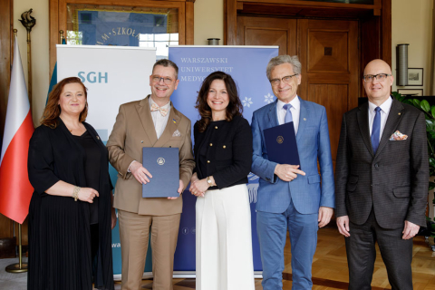 Five people standing side by side. From right: a woman in a black dress, next to her a man in a beige suit (Rector of SGH) holding a document of agreement, next to him a woman in a black jacket and white trousers, next to her a man in a blue suit (Rector of WUM) - holding a document of agreement, next to him a man in a dark suit. 