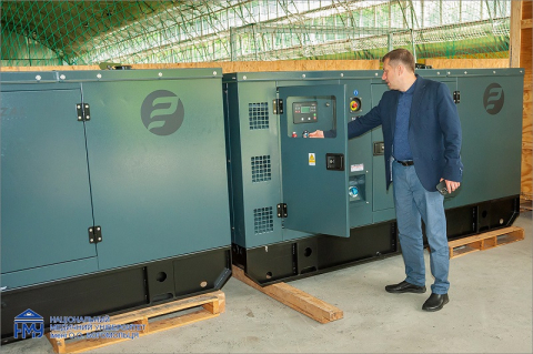 A man in jeans and a jacket turns a knob on a power generator