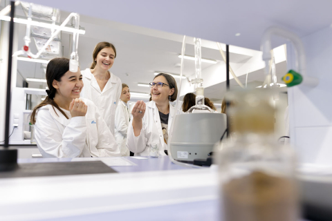 Two young girls and a middle-aged woman in white aprons in an analytical laboratory.