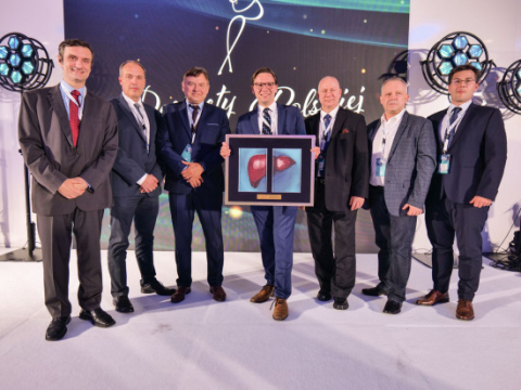 A group of standing men, dressed elegantly in suits, smile for the camera. The man in the middle holds a picture in a frame, a liver painted on the picture.