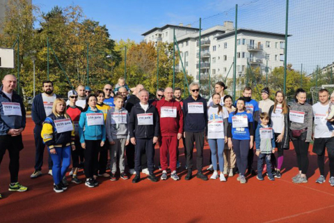 A group of people dressed in sportswear. They stand on the pitch and smile for the camera.