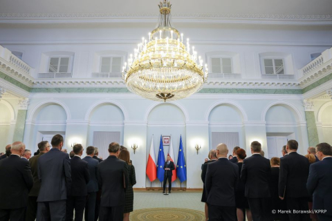 A room in the president's palace . At the end stands a man in a suit facing forward. The other people are standing facing backwards.